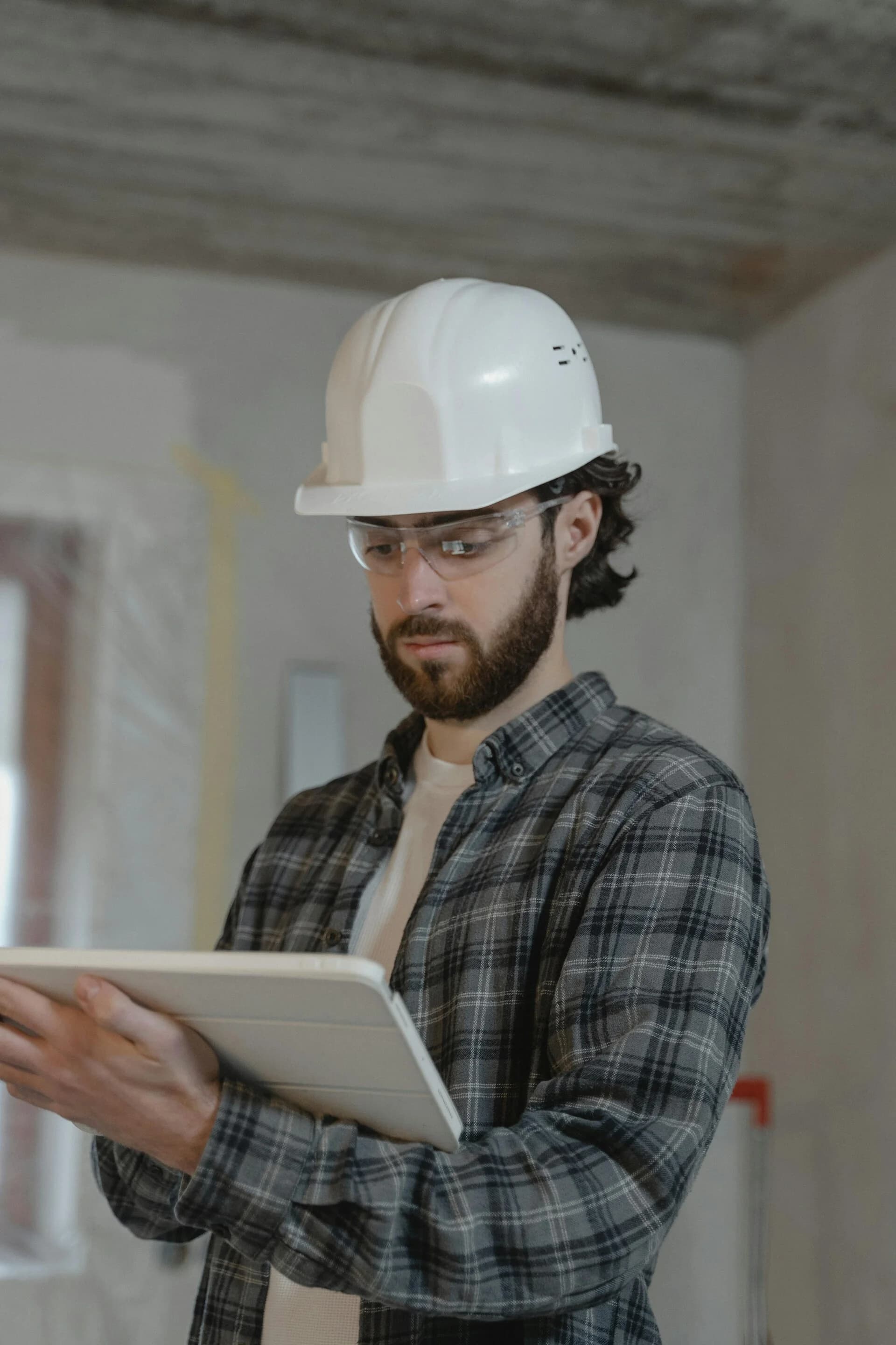 Uitvoerder met helm en tablet controleert werkzaamheden in een pand in aanbouw
